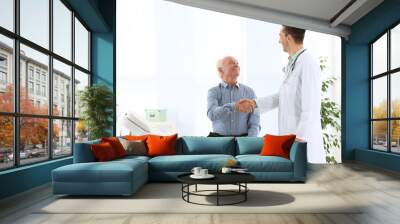 Doctor and elderly patient shaking hands in hospital. Space for text Wall mural