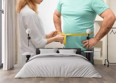 Doctor measuring overweight man's waist in hospital, closeup Wall mural