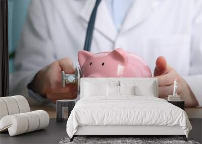 Doctor with piggy bank and stethoscope at wooden table, closeup Wall mural