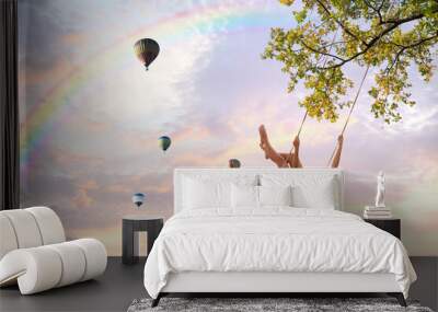 Dream world. Young woman swinging, hot air balloons in sunset sky on background Wall mural