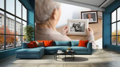 Elderly woman with framed family portrait at home Wall mural