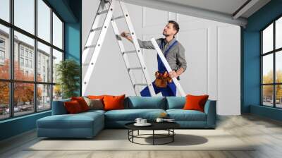 Electrician in uniform with ceiling lamp on metal ladder indoors Wall mural