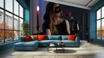 Elegant woman in black eye mask with rose at table indoors in evening Wall mural