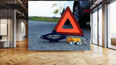 Emergency warning triangle, towing strap and scissor jack near car outdoors. Safety equipment Wall mural