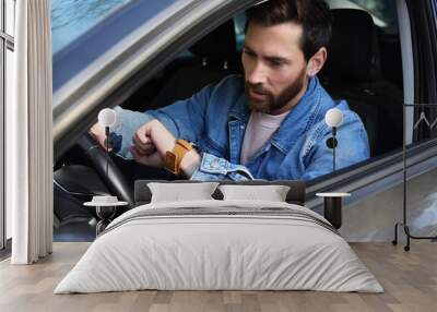 Emotional man checking time on watch in car. Being late concept Wall mural