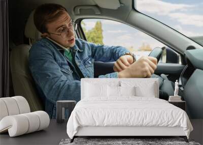 Emotional young man checking time while talking on phone in car. Being late Wall mural