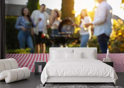 Empty table and blurred view of friends having barbecue party outdoors. Space for text Wall mural