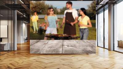 Empty wooden table and blurred view of friends cooking food on barbecue grill in park Wall mural