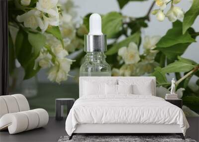 Essential oil in bottle and beautiful jasmine flowers on pale green background, closeup Wall mural