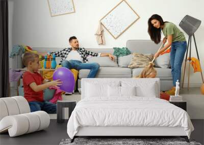 Exhausted mother trying to clean up mess made by children and lazy father in room Wall mural