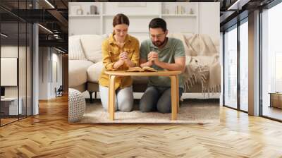 Family couple praying over Bible together at table indoors Wall mural