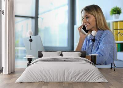 Female business trainer talking on phone while working with laptop in office Wall mural