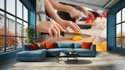 Female chef cutting paprika on wooden board at table, closeup Wall mural