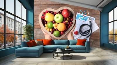 Female doctor holding plate with fresh fruits over wooden table, top view. Cardiac diet Wall mural