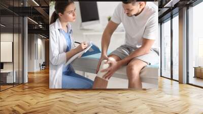 Female orthopedist examining patient with injured knee in clinic Wall mural