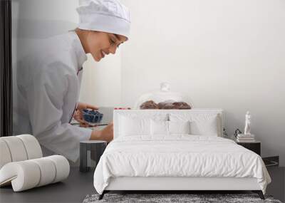 Female pastry chef decorating desserts with berries at table in kitchen Wall mural