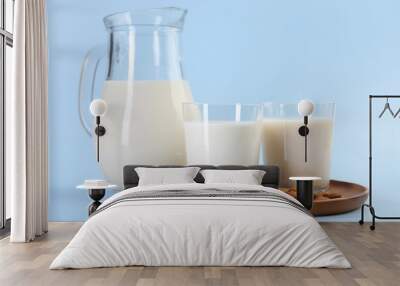 Fresh almond milk in glasses, jug and nuts on light blue background Wall mural