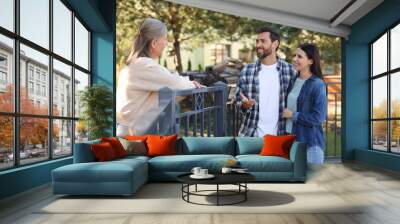 Friendly relationship with neighbours. Happy young couple talking to senior woman near fence outdoors Wall mural