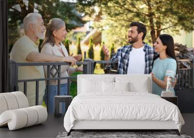 Friendly relationship with neighbours. Young family talking to elderly couple near fence outdoors Wall mural