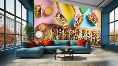 Friends holding delicious tacos on color background, top view Wall mural