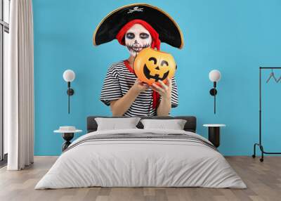 Funny boy with pumpkin bucket dressed like pirate on light blue background. Halloween costume Wall mural