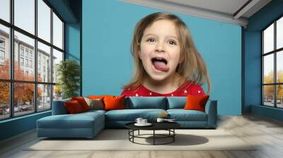 Funny little girl showing her tongue on light blue background Wall mural