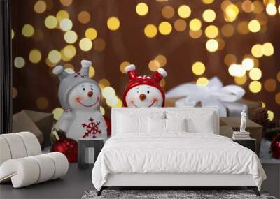 Funny snowman figure and other Christmas decor on artificial snow against blurred lights Wall mural