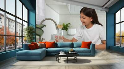 Girl filling glass with water from tap in kitchen Wall mural