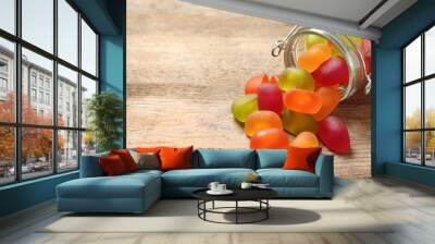 Glass jar and scattered jelly candies on wooden table, space for text Wall mural