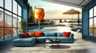 Glass of fresh summer cocktail on wooden table near swimming pool outdoors at sunset. Space for text Wall mural