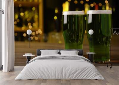 Glasses of green beer on wooden table against blurred lights, space for text. St Patrick's Day celebration Wall mural