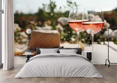 Glasses of rose wine and straw hat on white wooden table outdoors. Space for text Wall mural