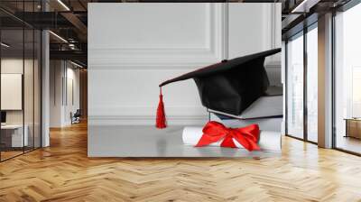 Graduation hat, books and diploma on floor near white wall, space for text Wall mural