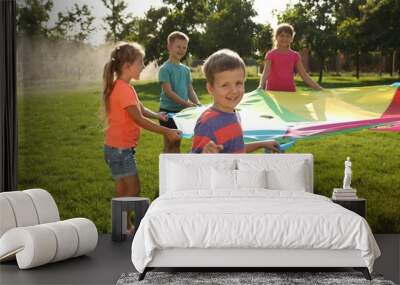 Group of children playing with rainbow playground parachute on green grass. Summer camp activity Wall mural