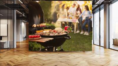 Group of friends having party outdoors. Focus on barbecue grill with food. Space for text Wall mural