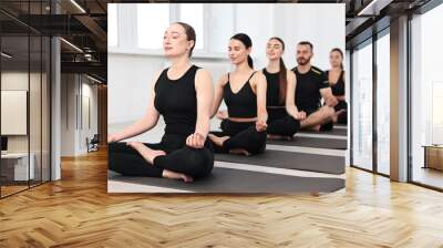 Group of people meditating on mats in yoga class Wall mural