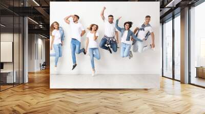 Group of young people in jeans jumping near light wall Wall mural