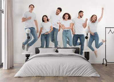 Group of young people in stylish jeans jumping near white wall Wall mural