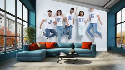 Group of young people wearing T-shirts with letters near light wall. Christian religion Wall mural