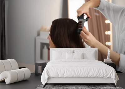 Hairdresser working with woman using curling hair iron in salon Wall mural