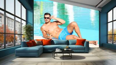 Handsome young man lying near swimming pool on sunny day Wall mural