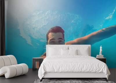 Handsome young man swimming in pool, underwater view Wall mural