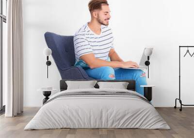 Handsome young man with laptop in armchair on white background Wall mural