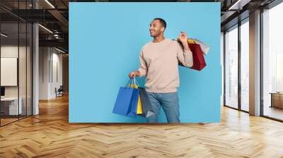 Happy African American man with shopping bags on light blue background Wall mural