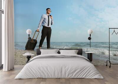 Happy businessman with suitcase walking on beach. Business trip Wall mural