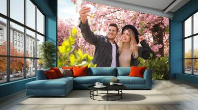 Happy couple taking selfie near blossoming sakura outdoors on spring day Wall mural