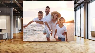 Happy family having fun on sandy beach near sea at sunset Wall mural