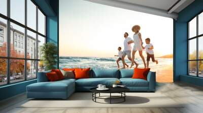 Happy family running on sandy beach near sea at sunset Wall mural