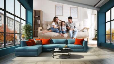 Happy family with little daughter sitting on sofa in living room Wall mural