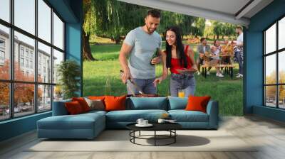 Happy friends cooking meat and vegetables on barbecue grill in park Wall mural